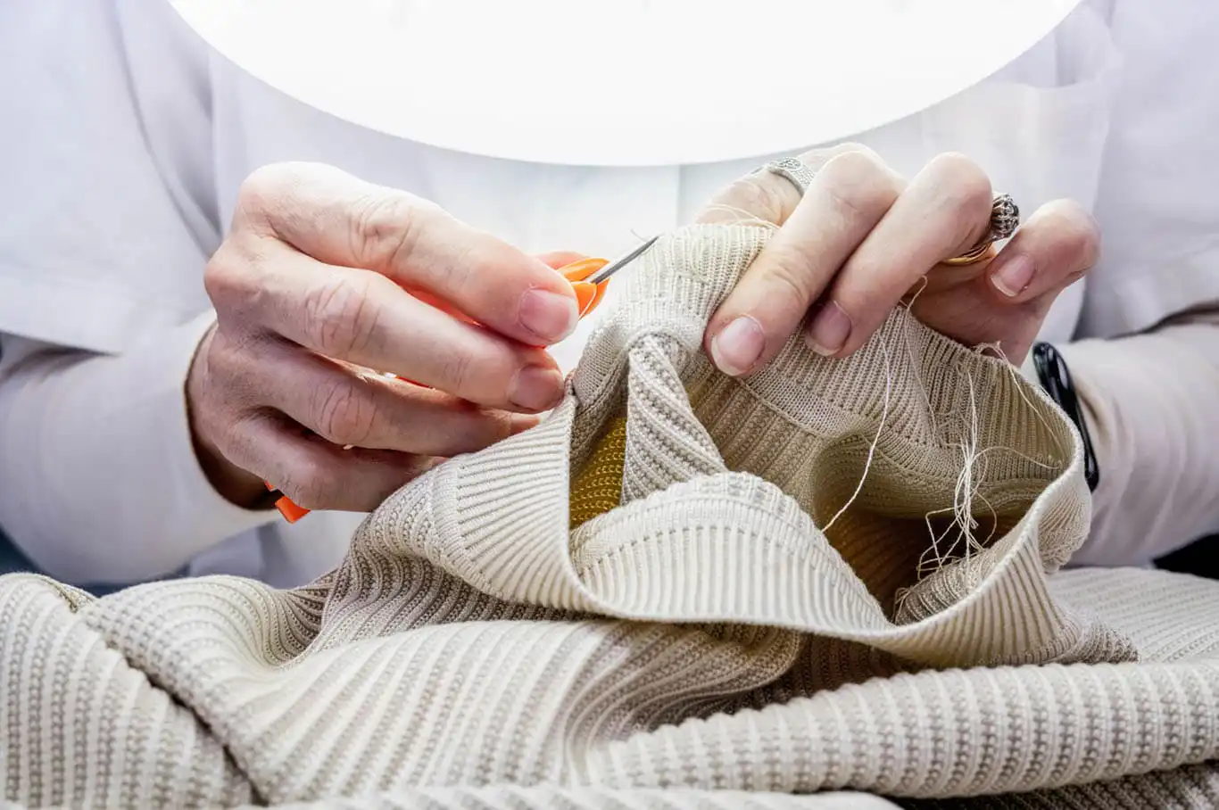 Hands linking the ribbed collar of a cream sweater in an Italian knitwear workshop