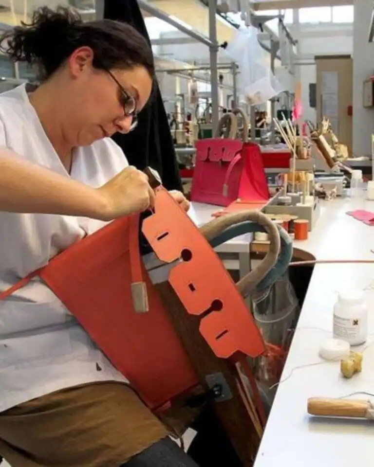 An artisan assembling a red leather bag in an Italian workshop