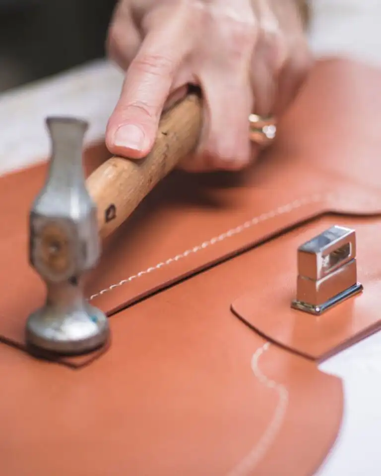An artisan hammering a stitched leather panel flat