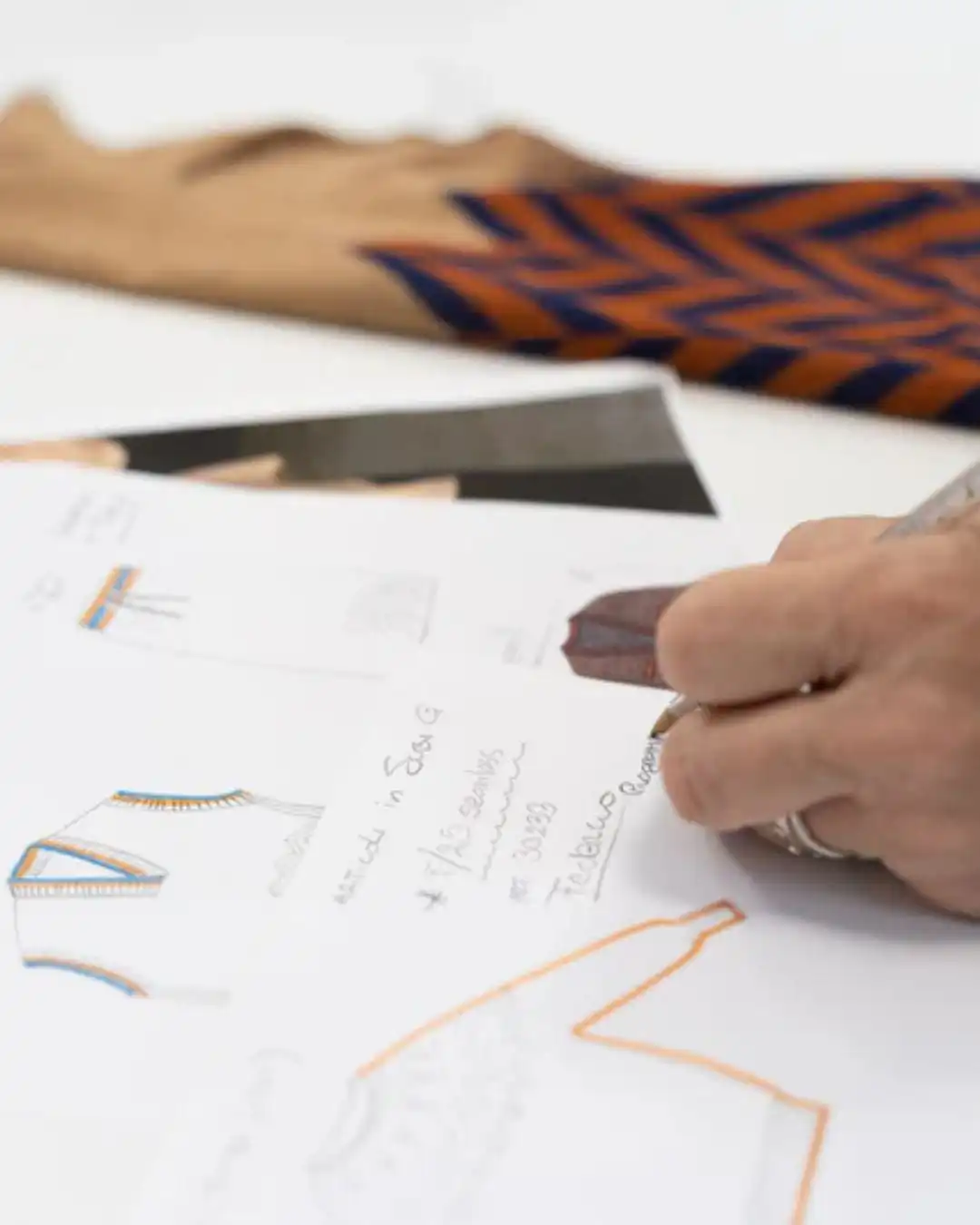 A designer sketching a garment on paper next to a fabric swatch, in an Italian studio