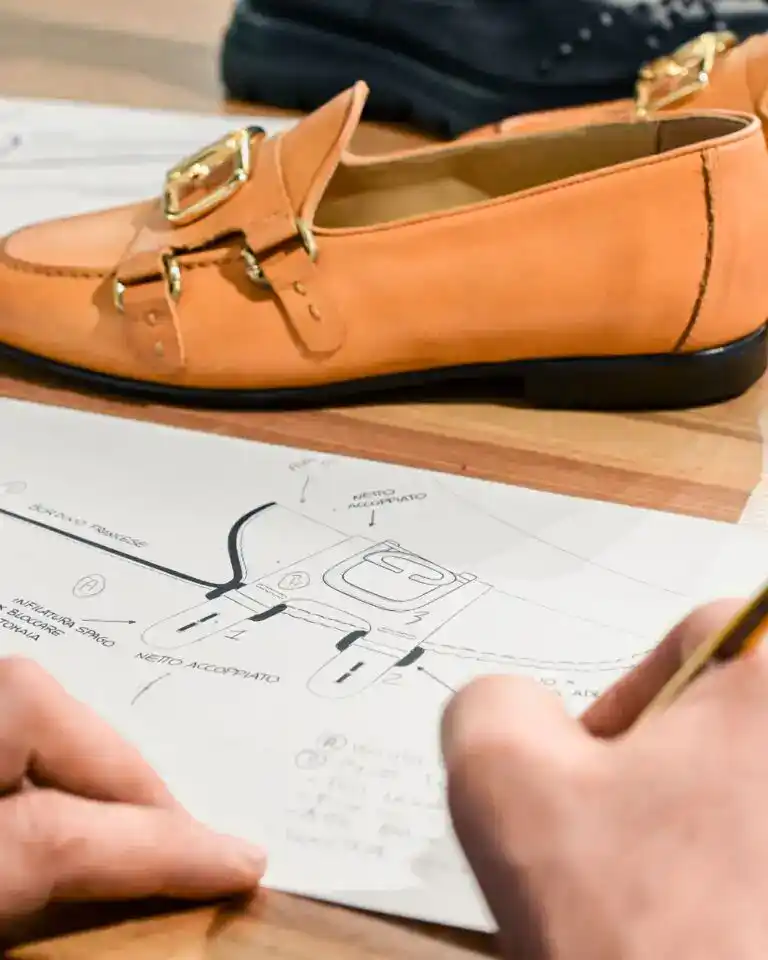 A leather loafer on its paper pattern while a designer marks up the drawing