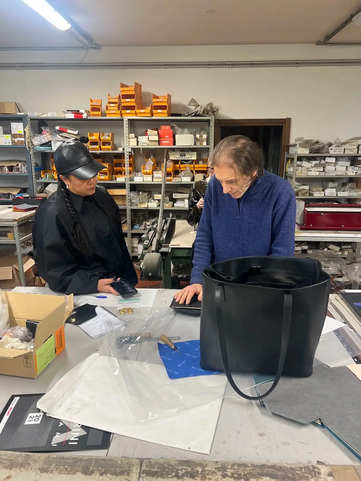 Inside the leather workshop outside Milan: two artisans review a finished Rebekah tote at the cutting table