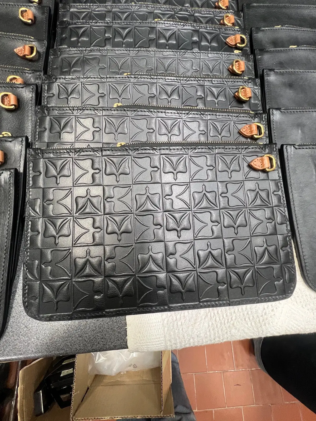 Rows of embossed Heritage Dove clutch panels with brass hardware, laid out for assembly