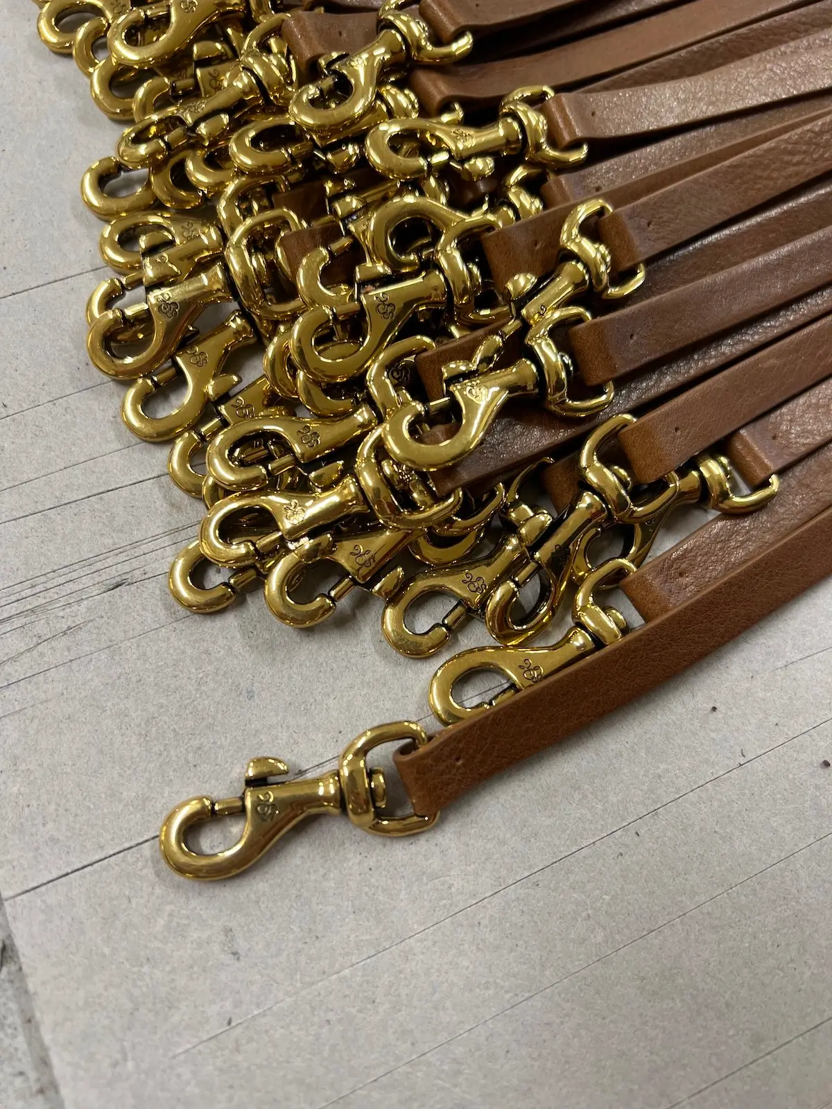 Brass snap hooks and zip pulls for Maison Veni, engraved and plated, laid out before assembly