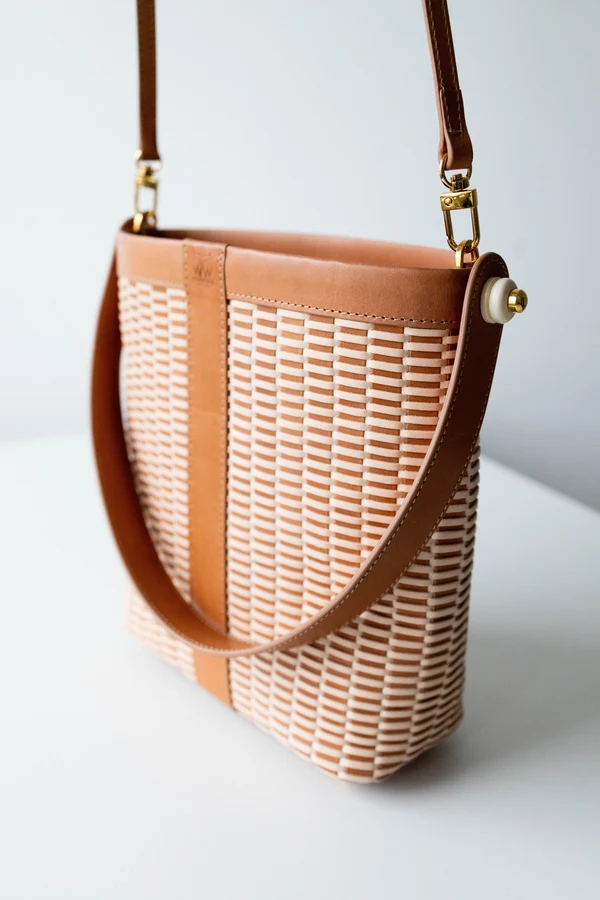 The woven leather bucket bag hanging by its strap against a white wall