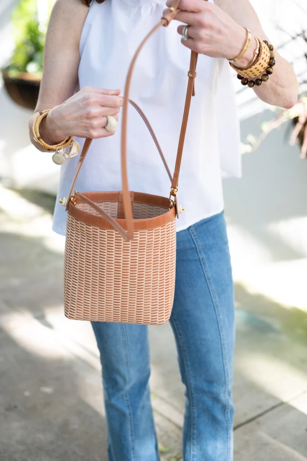 A woman in a white top holds the woven leather bucket bag by its strap