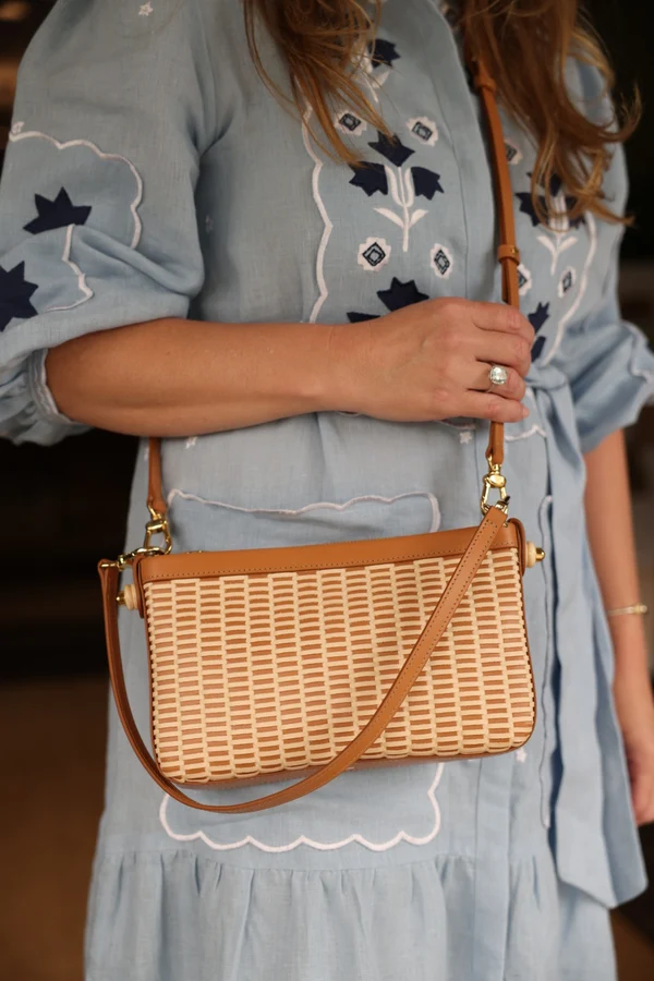The woven leather clutch worn crossbody over a blue embroidered dress