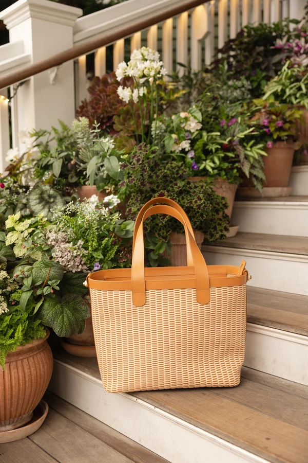 The woven leather tote on the steps of a porch surrounded by hydrangeas