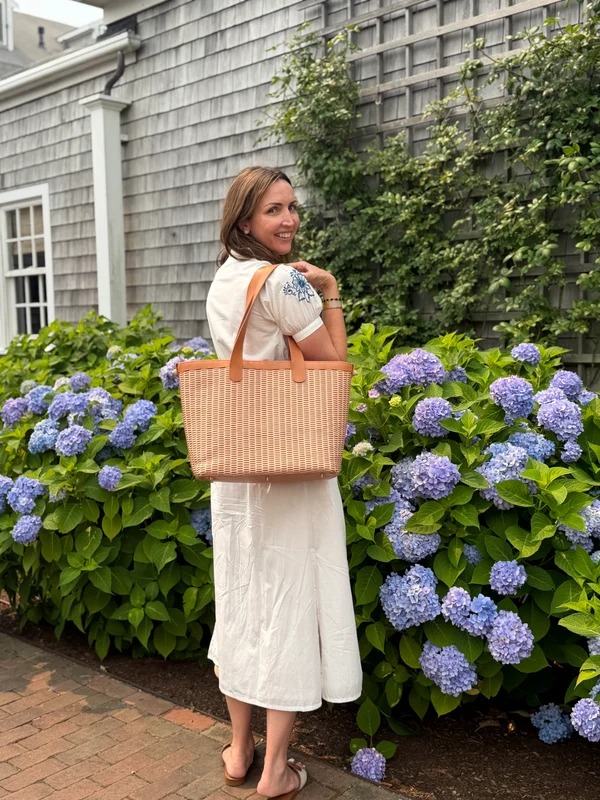 A woman carries the woven leather tote past a hydrangea hedge in Nantucket