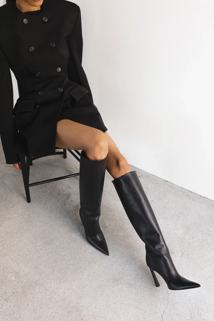 A model in a black dress wears Hagelstam black knee-high leather boots