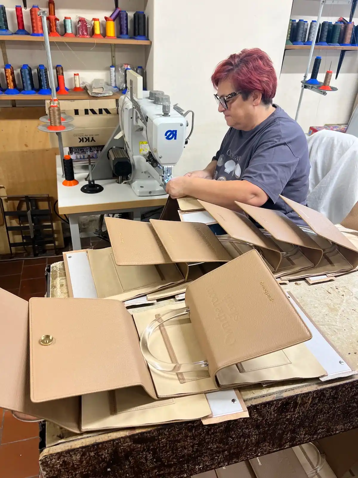 An artisan at a sewing machine in the workshop with cut leather pieces for the quietBossy bags