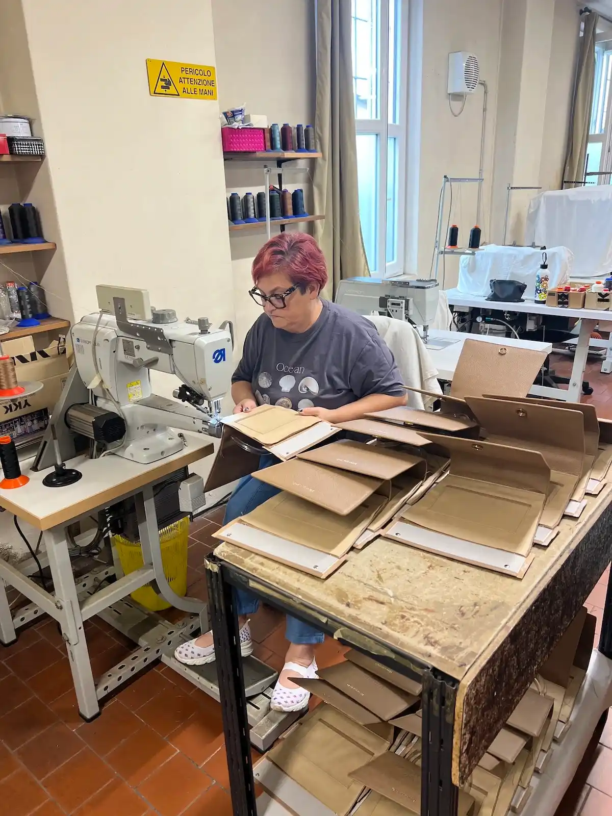 The leather workshop outside Milan: an artisan at the sewing station surrounded by thread spools and cut components