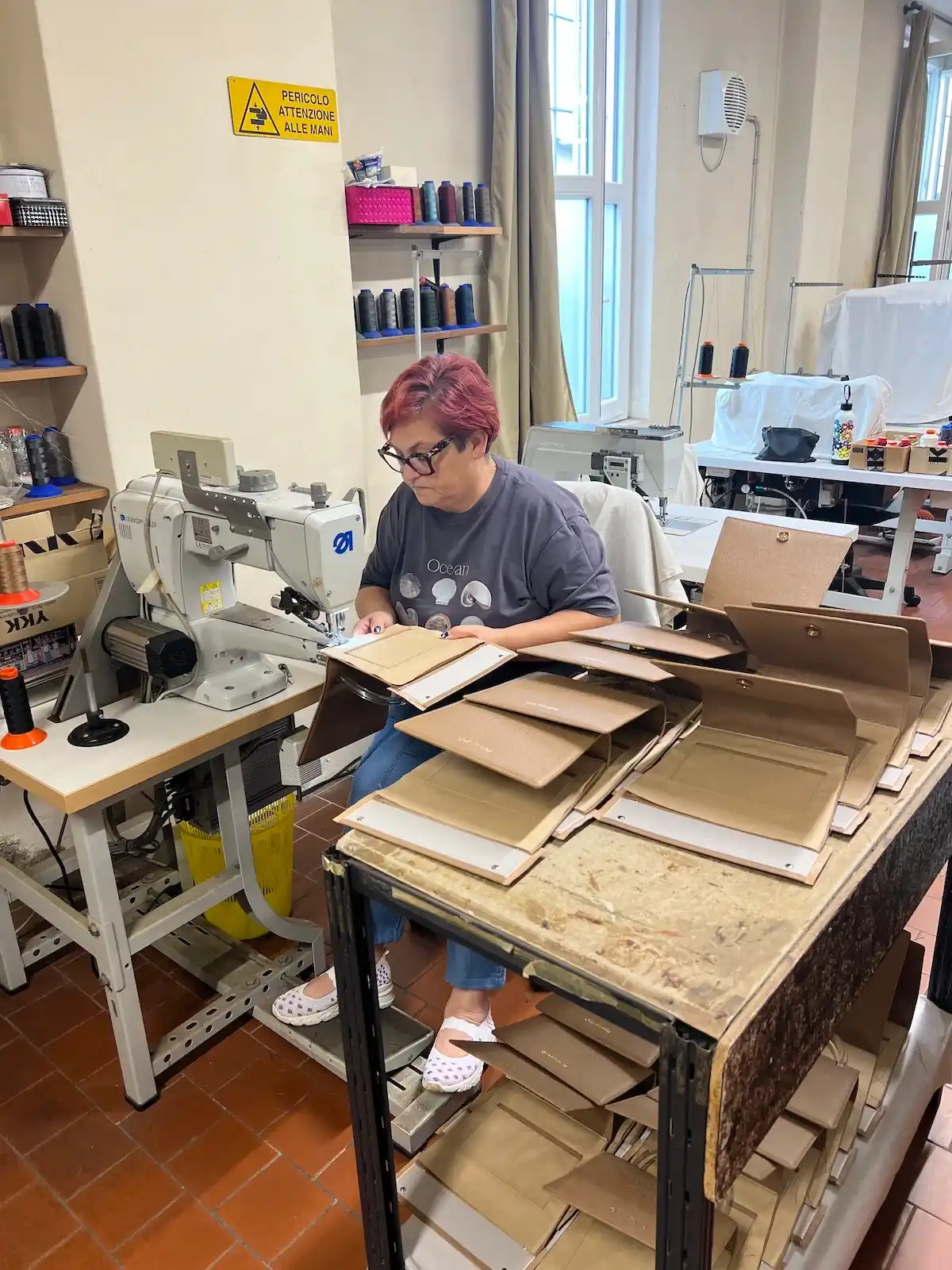 An artisan assembling leather components at an industrial sewing machine in the workshop