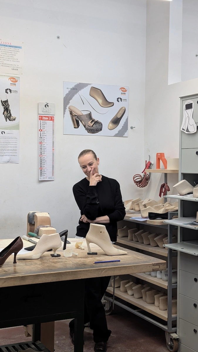 Sandra Hagelstam at the atelier's pattern table with sample shoes and sketches on the wall
