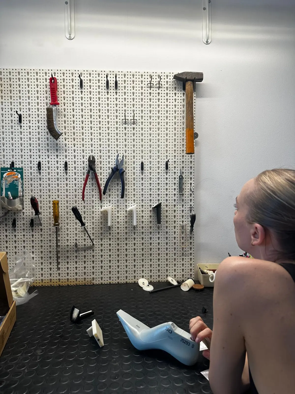 Sandra Hagelstam examines a shoe last in the atelier, in front of a wall of shoemaking tools