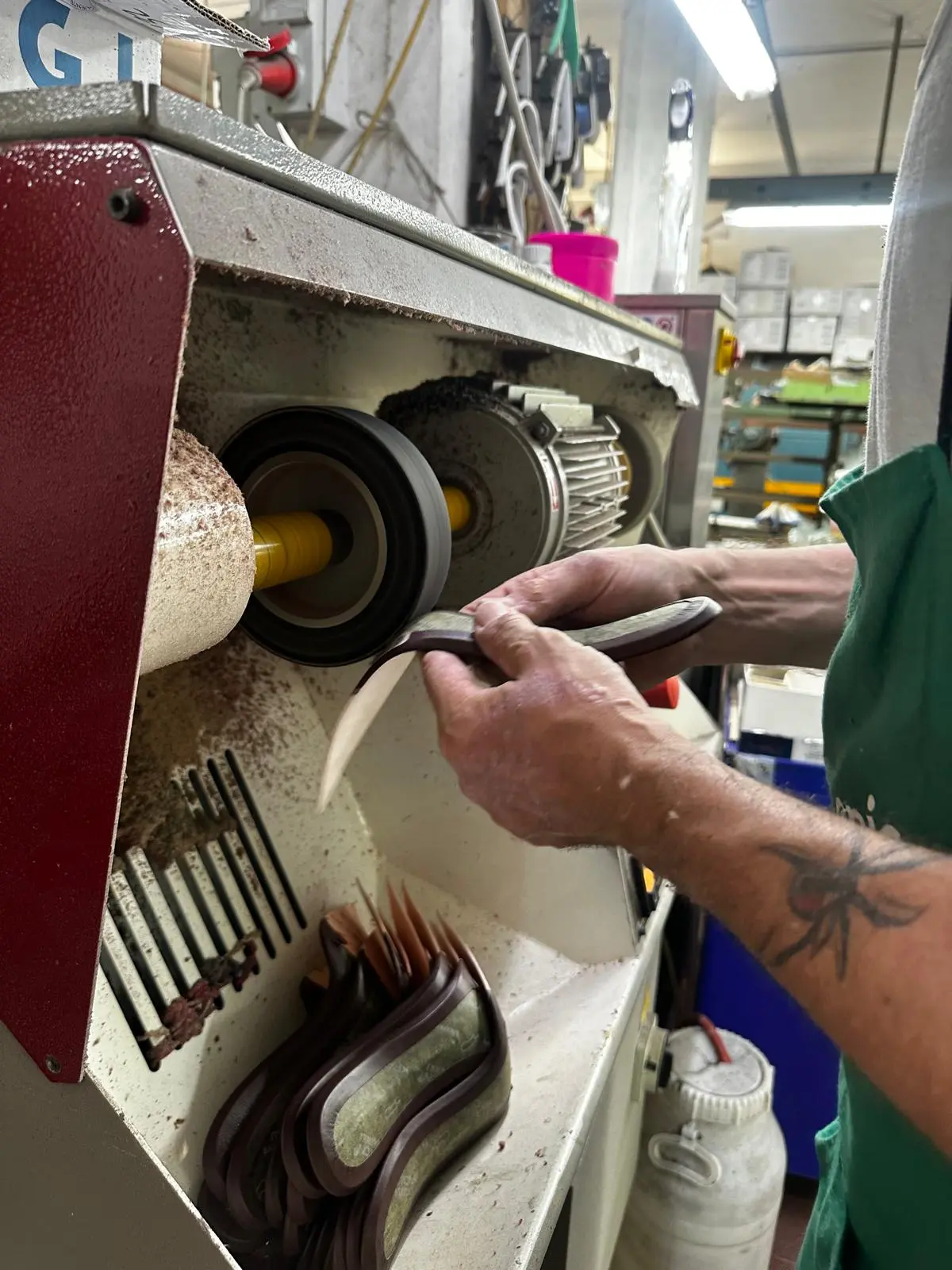 An artisan finishes a stack of sculpted heels on a buffing wheel at the heel factory